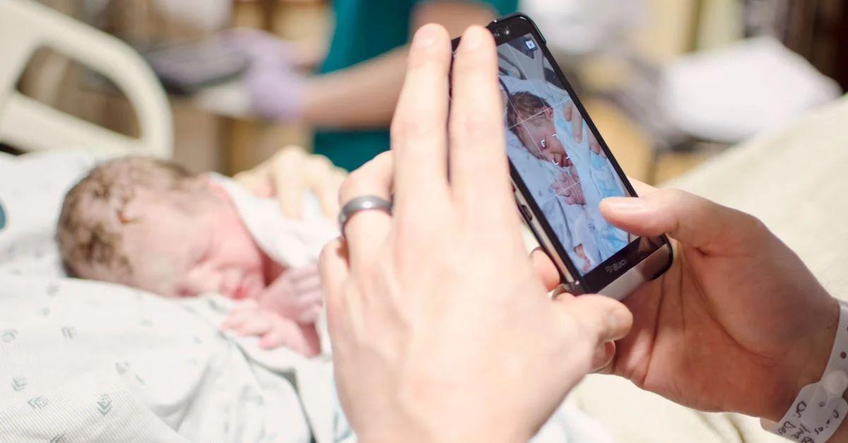Una foto en primer plano de un recién nacido siendo fotografiado con un smartphone en un entorno hospitalario.