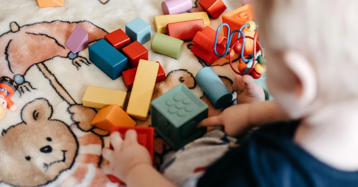 Un niño pequeño jugando alegremente con una variedad de bloques de construcción coloridos sobre una manta estampada.