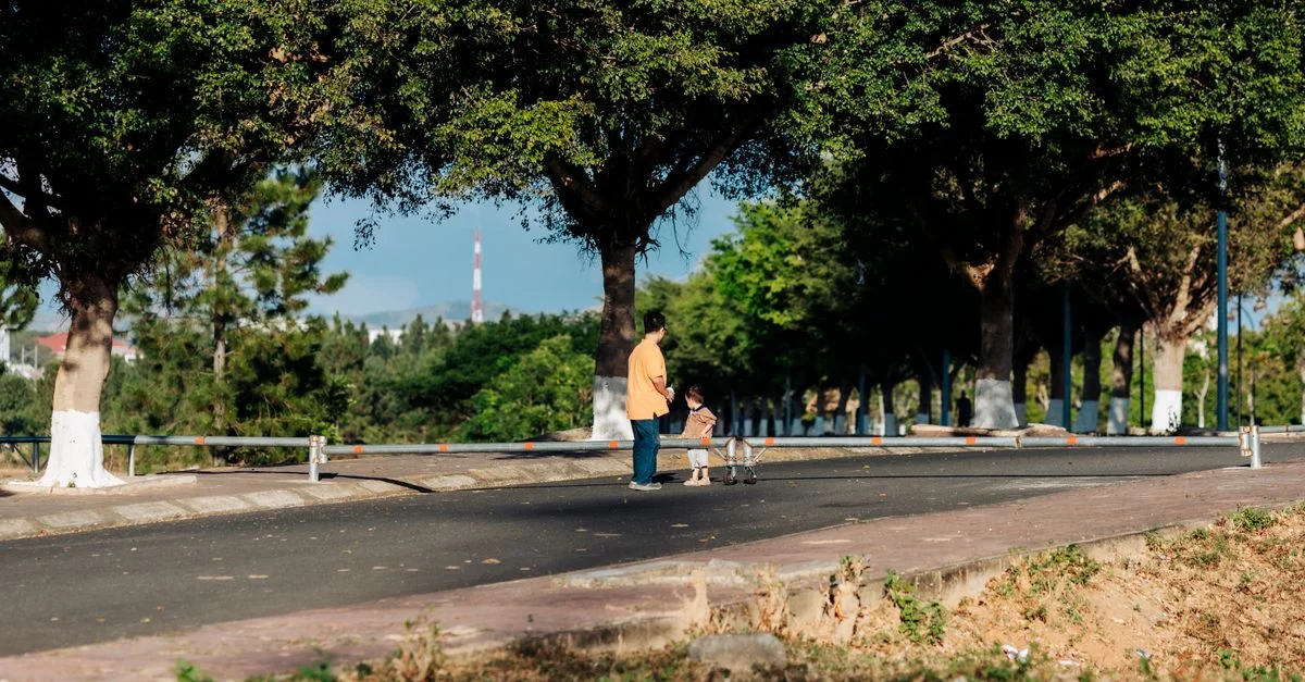 Una escena pacífica de un padre y un hijo paseando bajo árboles frondosos en Kon Tum.