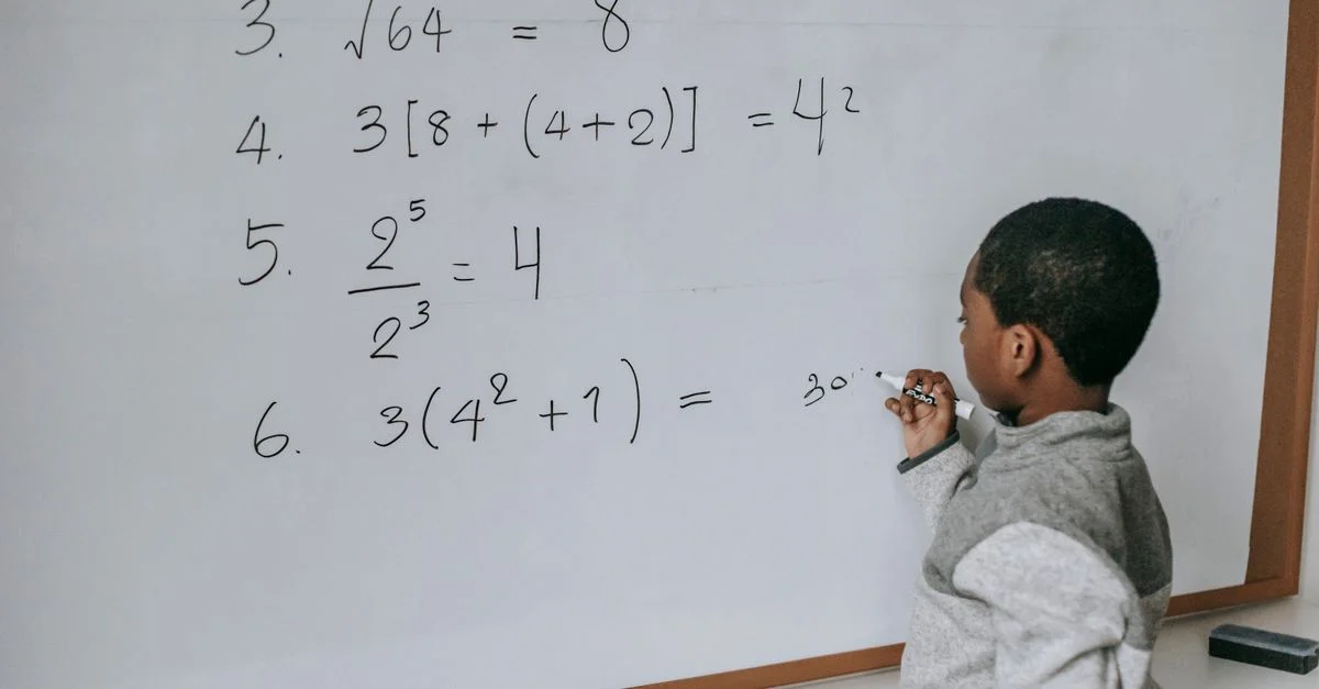 Un niño enfocado resuelve problemas matemáticos en una pizarra de aula, demostrando aprendizaje y concentración.