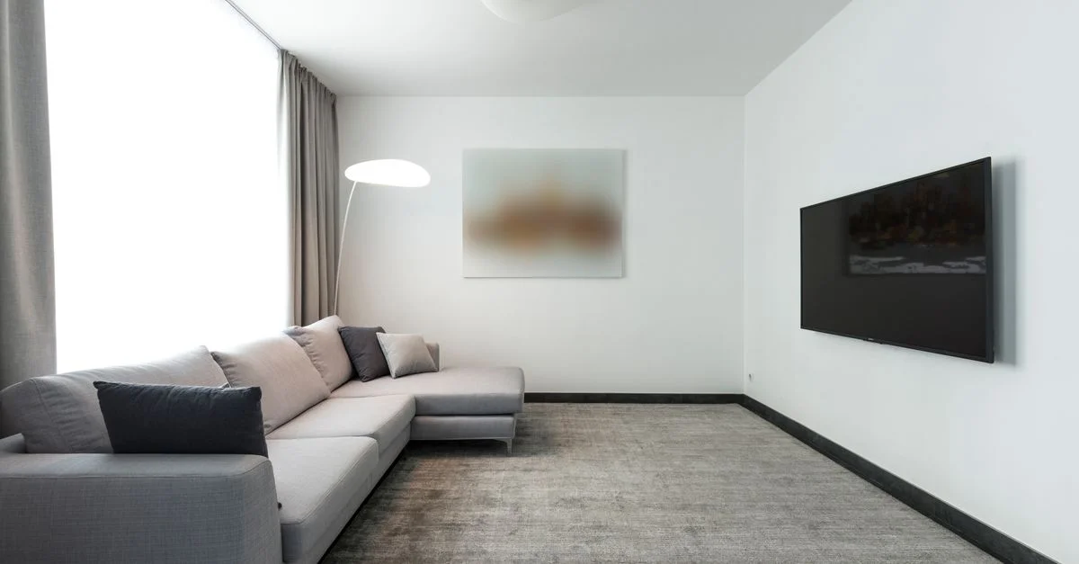 Sala de estar contemporánea con un sofá seccional gris y un televisor montado en la pared.
