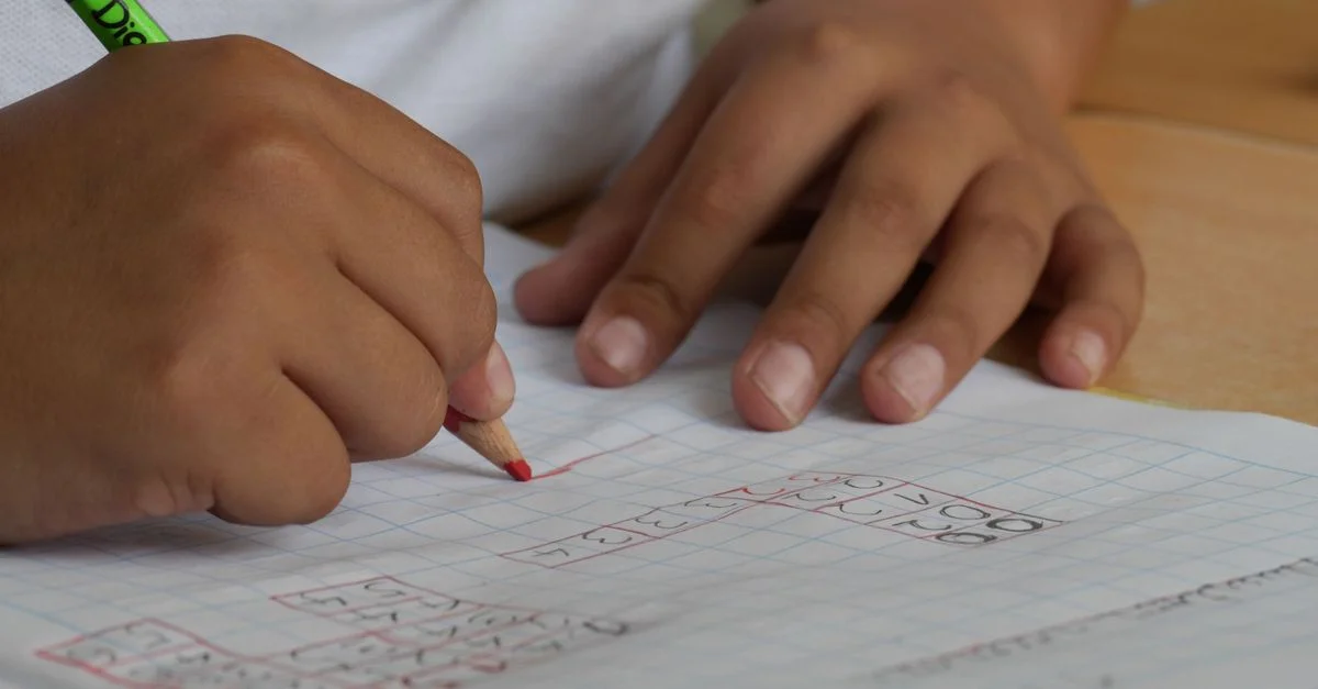 Primer plano de un estudiante escribiendo ecuaciones matemáticas en un cuaderno con un lápiz en interiores.