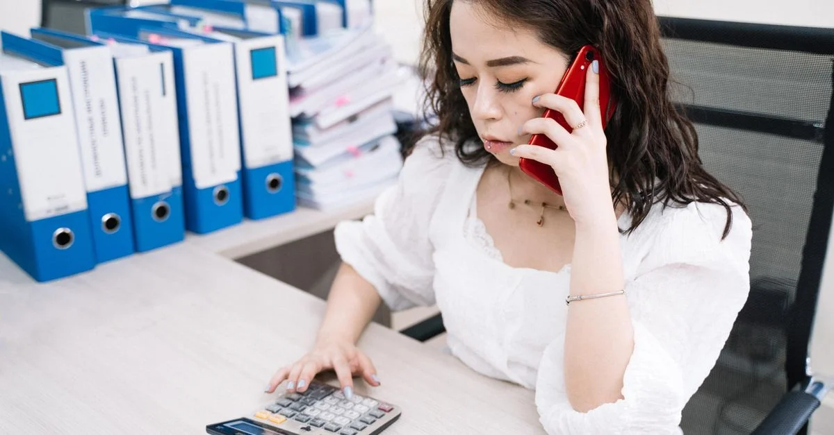 Mujer de negocios multitarea con calculadora y teléfono móvil en el escritorio.