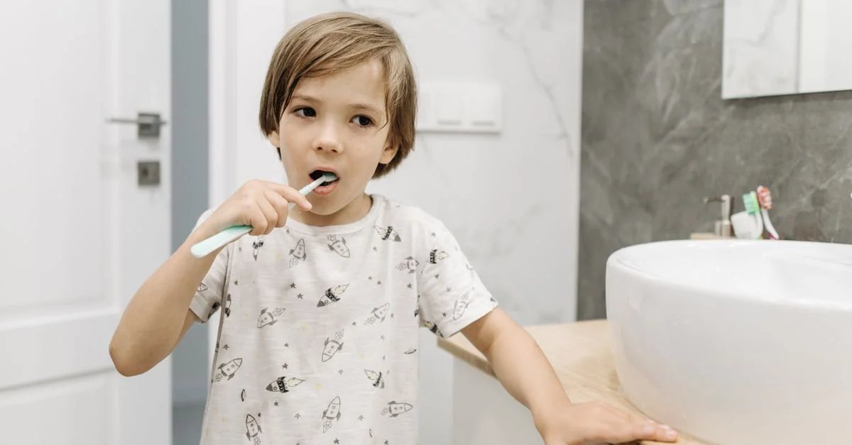 Un jeune garçon blond pratiquant l'hygiène dentaire en se brossant les dents à l'intérieur.