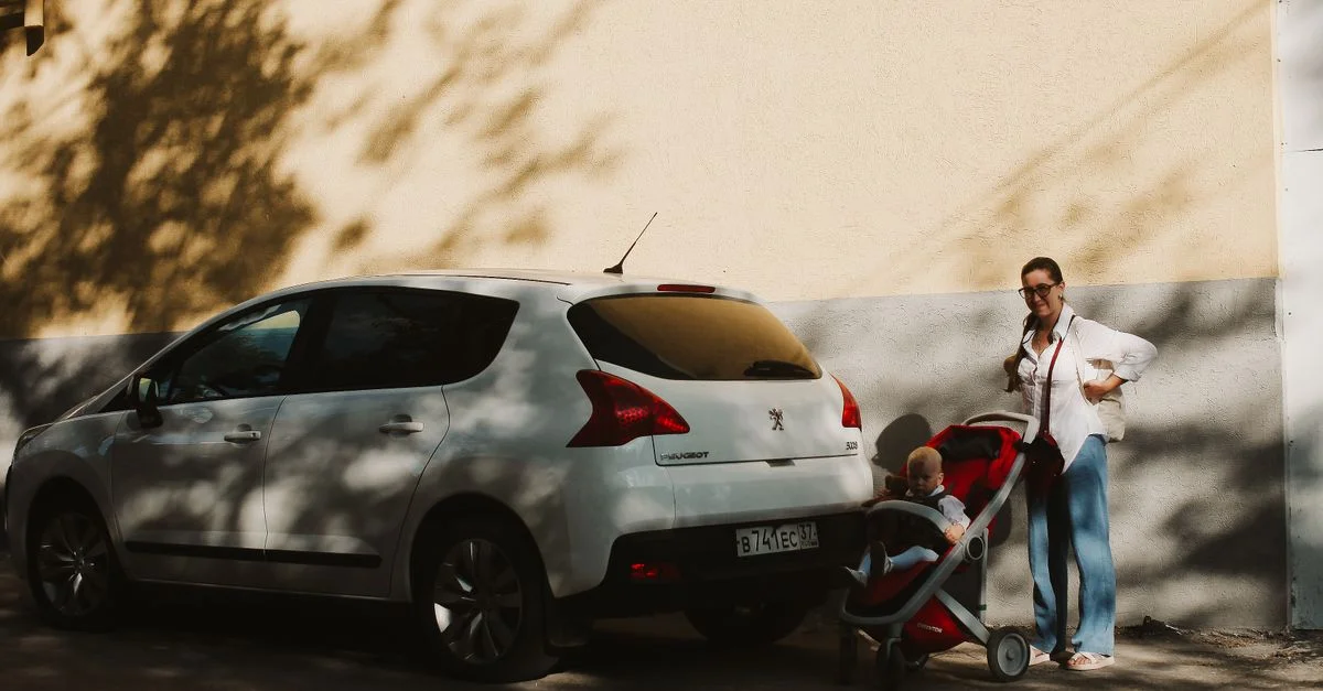 Madre con carrito y niño al lado de un coche blanco en una calle soleada.