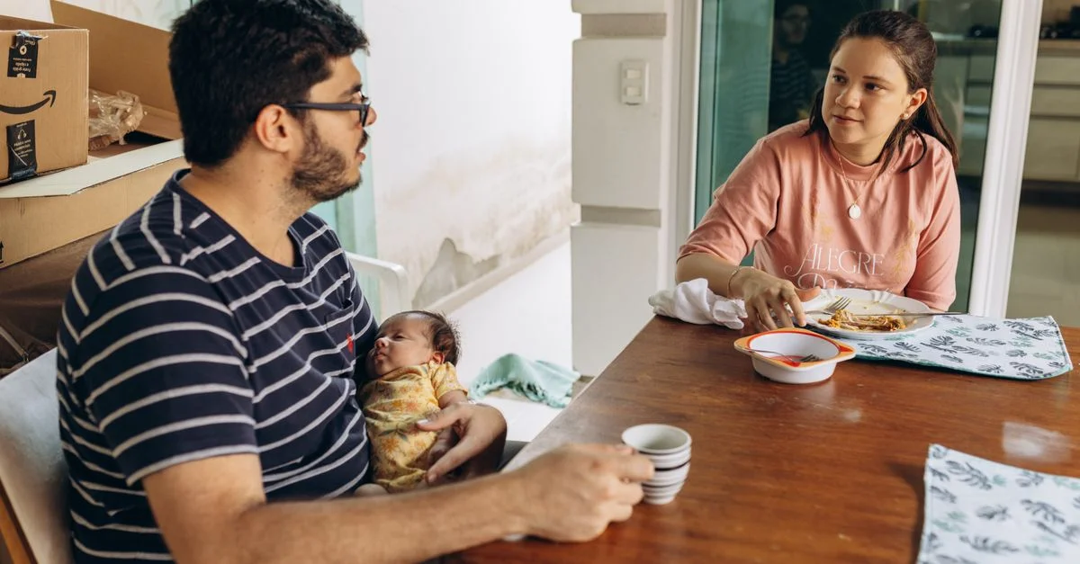 Una joven pareja disfruta de una comida en casa con su bebé sentado en la mesa del comedor.