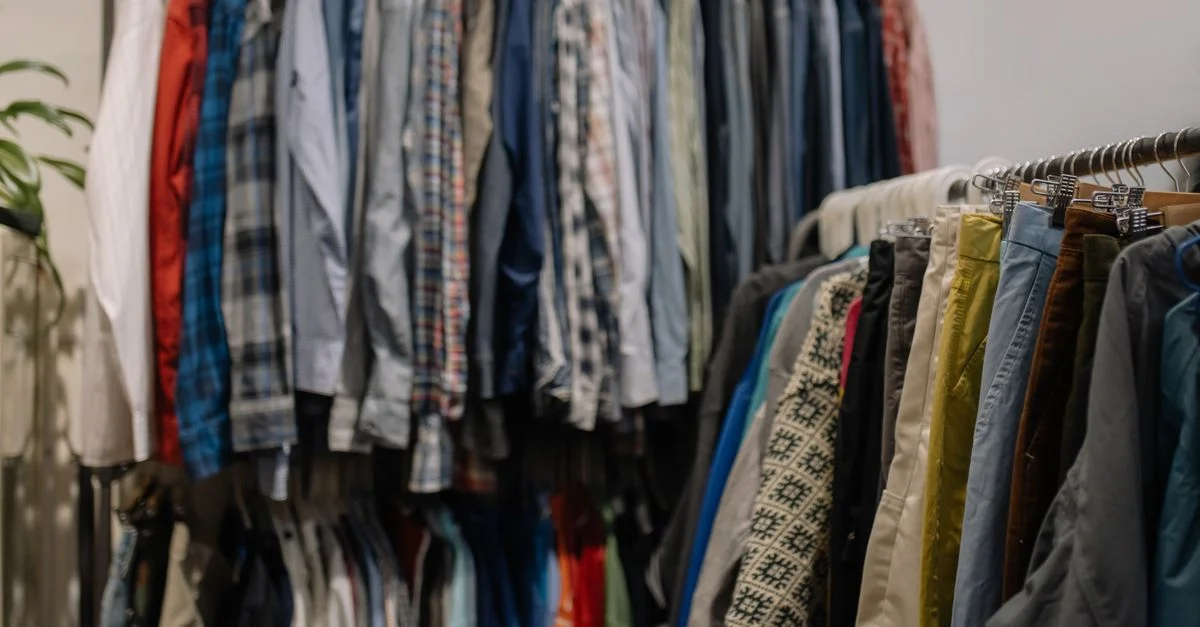 Ropa variada en percheros en una tienda de segunda mano, mostrando diferentes estilos y colores.