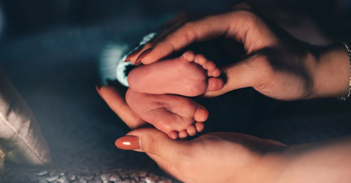 Acercamiento de una madre sosteniendo suavemente los pies de un recién nacido, simbolizando cuidado y amor.