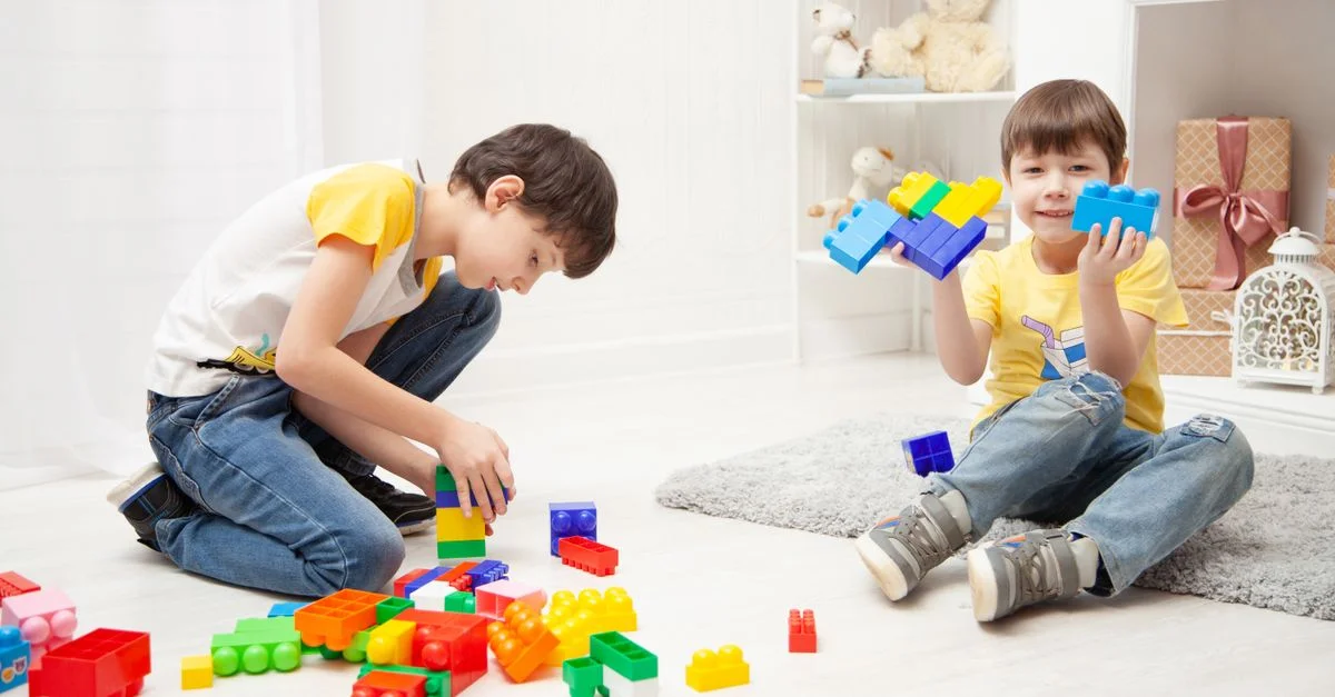 Dos niños jugando alegremente con bloques de construcción coloridos en una habitación interior luminosa.