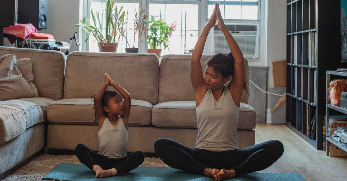 Una madre y su hija practicando yoga en su sala de estar, abrazando el fitness y el vínculo familiar.
