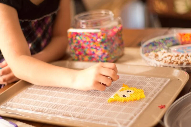 Un niño creando un diseño vibrante en un tablero de clavijas con cuentas coloridas, fomentando la creatividad y el juego.