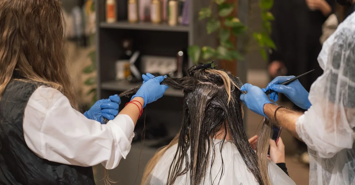 Des stylistes professionnels teignent les cheveux d'une femme dans un salon moderne, illustrant le travail d'équipe et l'expertise.