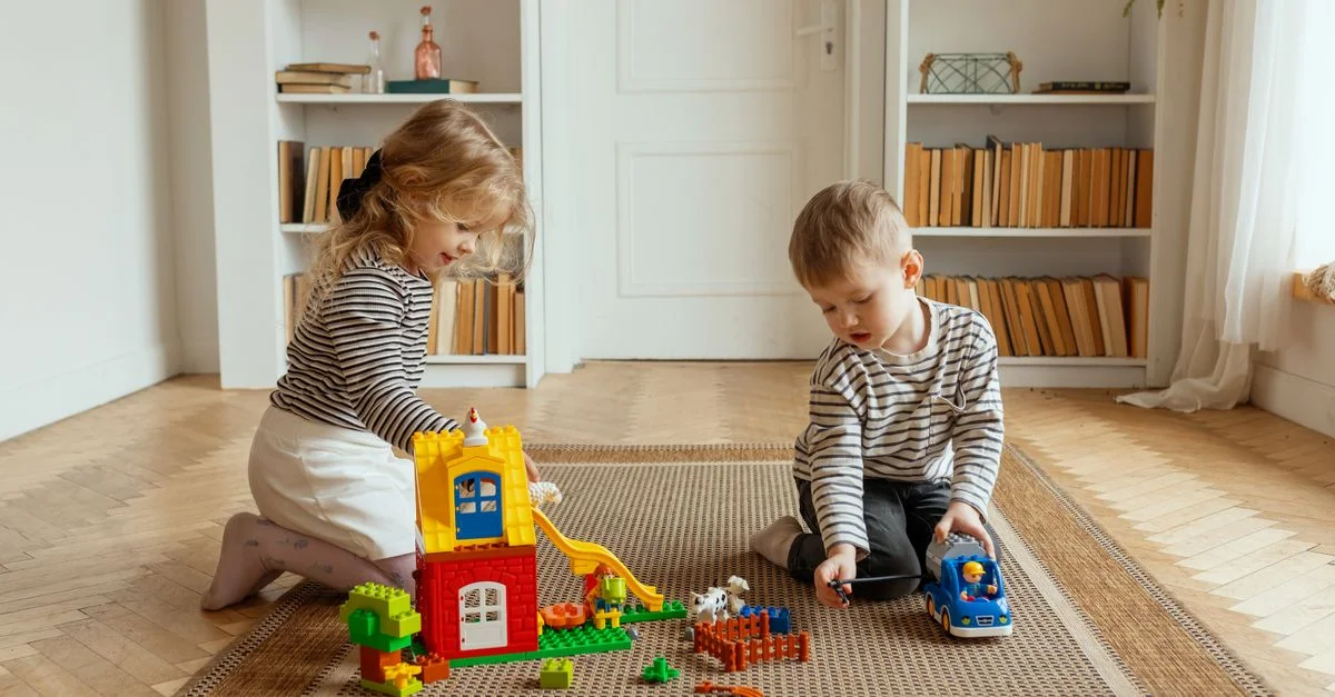 Dos niños construyendo y jugando con bloques coloridos en interiores, creando una atmósfera juguetona y cálida.