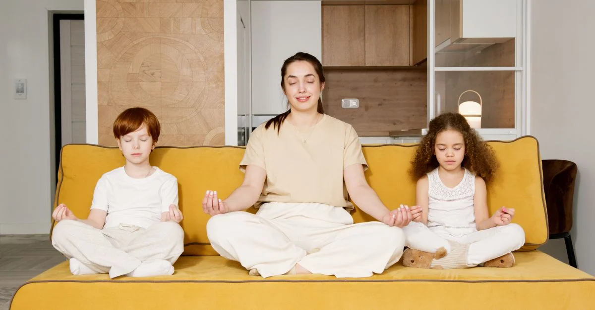 Una mujer y dos niños meditando juntos en un sofá, abrazando la atención plena familiar.