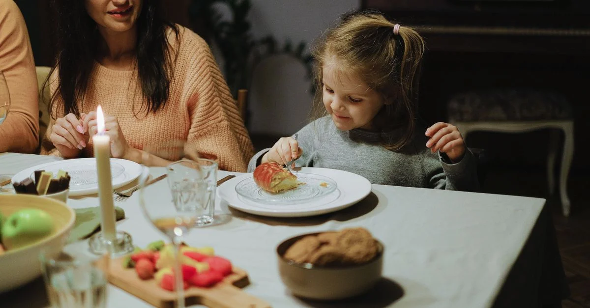 Una niña disfruta de un postre en la mesa de la cena familiar, creando una atmósfera hogareña.