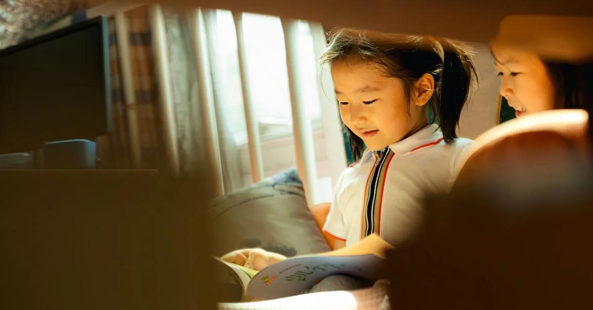 Dos niños leyendo libros con alegría junto a una ventana iluminada por el sol, fomentando el amor por el aprendizaje y la imaginación.