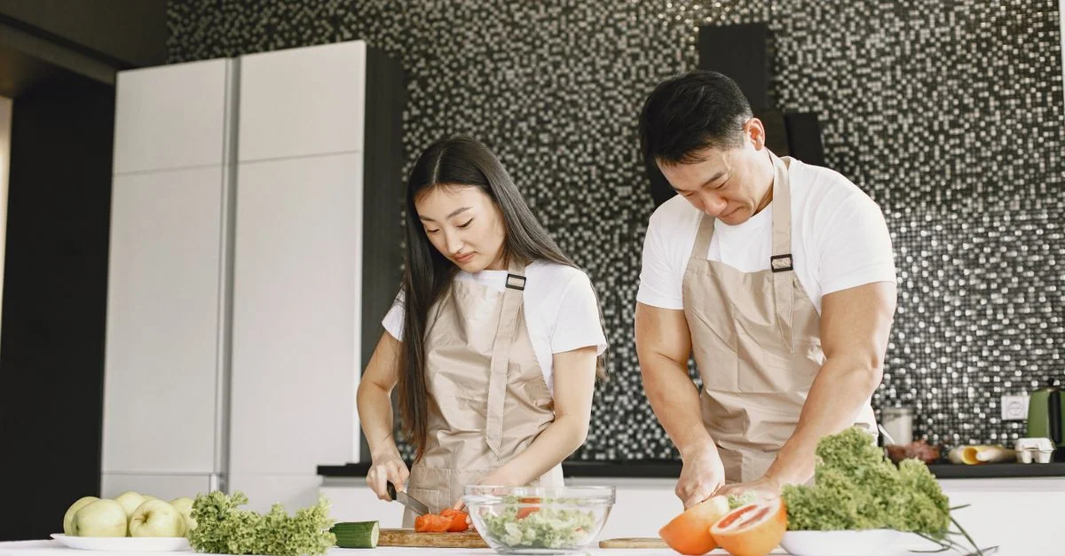 Pareja asiática preparando una comida saludable juntos en una cocina moderna, cortando verduras frescas.