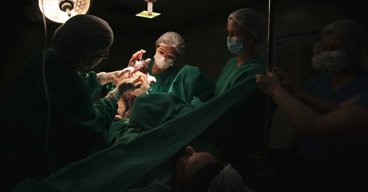 Médicos y enfermeras entregando un bebé recién nacido bajo luces quirúrgicas en un hospital.