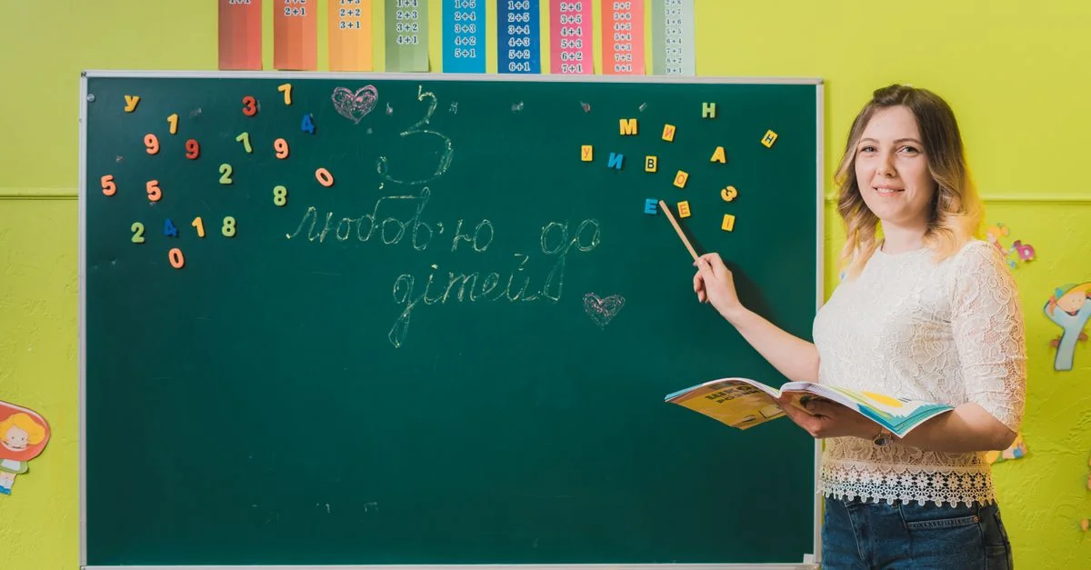 Una profesora señalando un pizarra con números en un aula colorida.