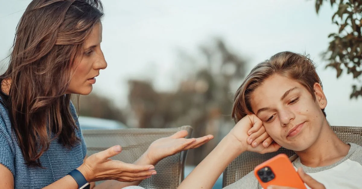 Une mère parlant à son fils adolescent tenant un smartphone à l'extérieur.