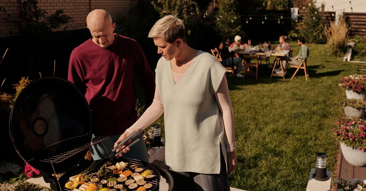 Pareja asando verduras en una reunión de barbacoa en el jardín.