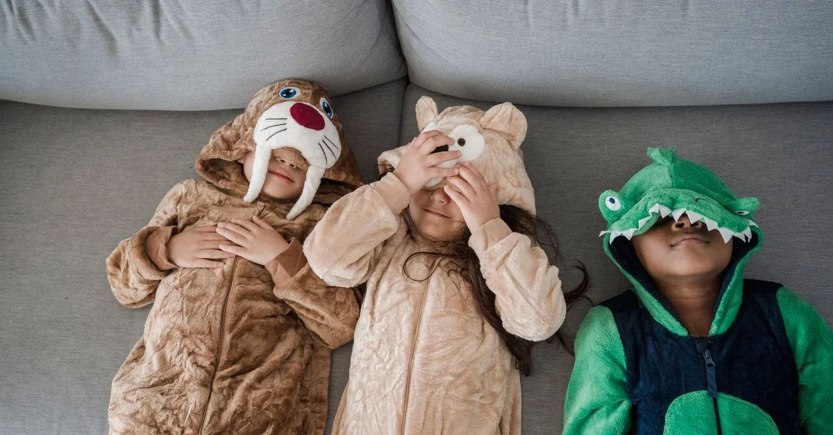 Tres niños en pijamas de animales tumbados en un sofá, mostrando un momento divertido y juguetón.