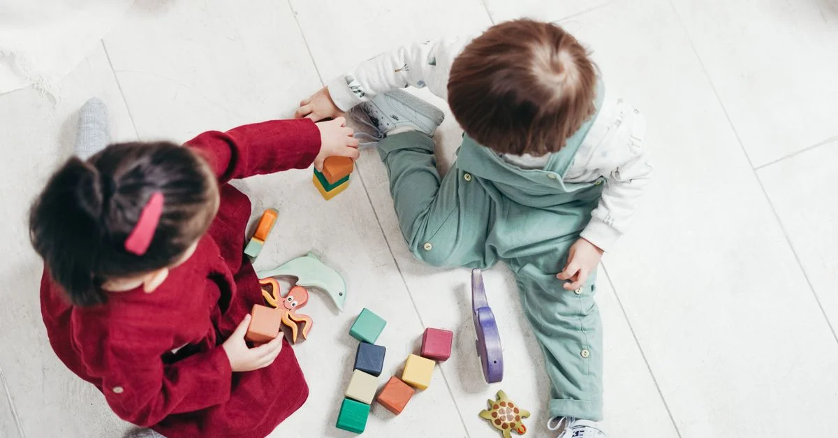 Dos niños pequeños interactuando con bloques de madera coloridos en interiores, fomentando la creatividad y la diversión.