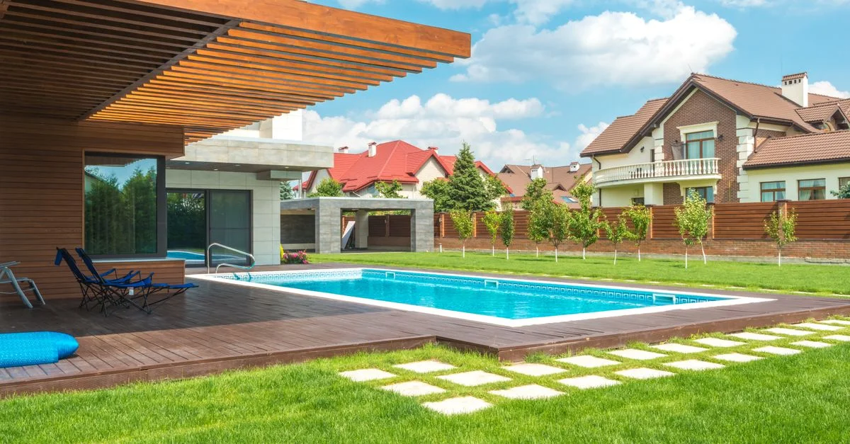 Impresionante exterior de casa moderna con piscina y patio bien cuidado bajo un cielo azul.