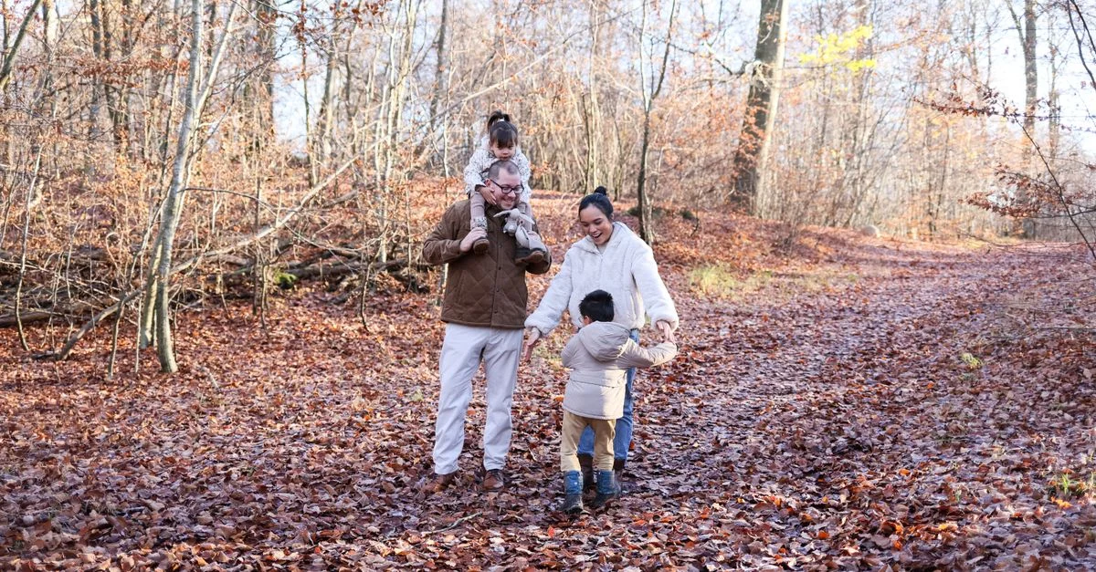 Familia feliz caminando junta por un sendero del bosque rodeado de hojas de otoño.