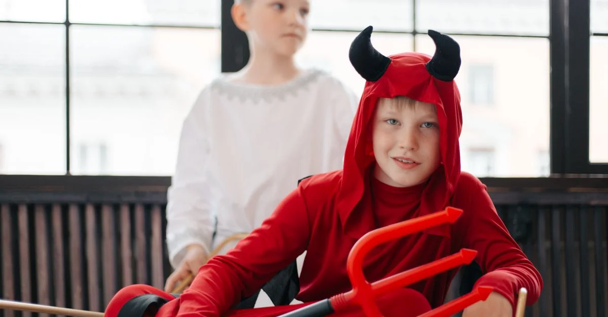 Dos niños en disfraces de ángel y diablo disfrutando de una celebración de Halloween en interiores.