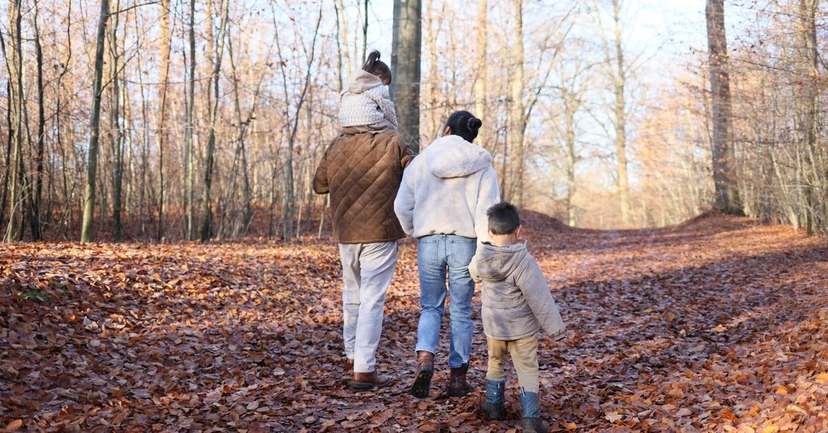 Una familia disfruta de un paseo por un bosque en otoño, rodeada de hojas caídas.
