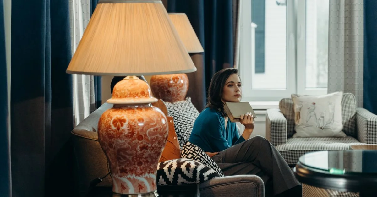 Femme se relaxant avec un livre dans un salon élégant et cosy. Décor raffiné et éclairage serein.
