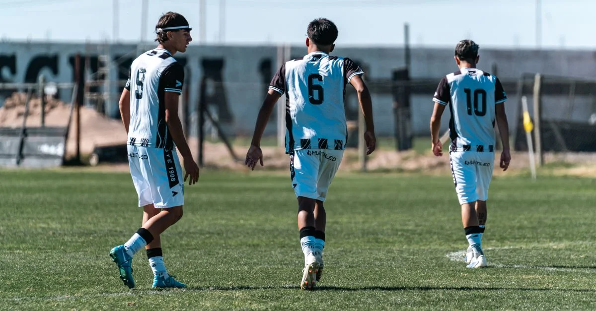 Tres jugadores de fútbol con camisetas blancas y negras caminando por un campo de hierba durante el día.