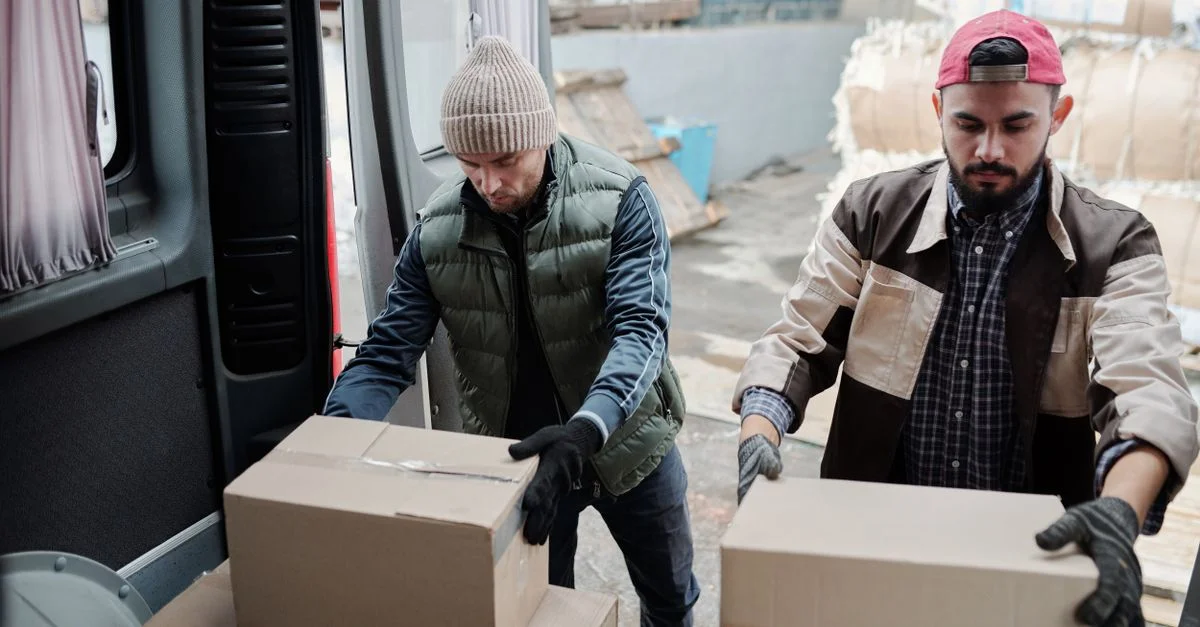 Dos trabajadores masculinos cargando paquetes en una furgoneta de entrega, trabajo en equipo en logística.