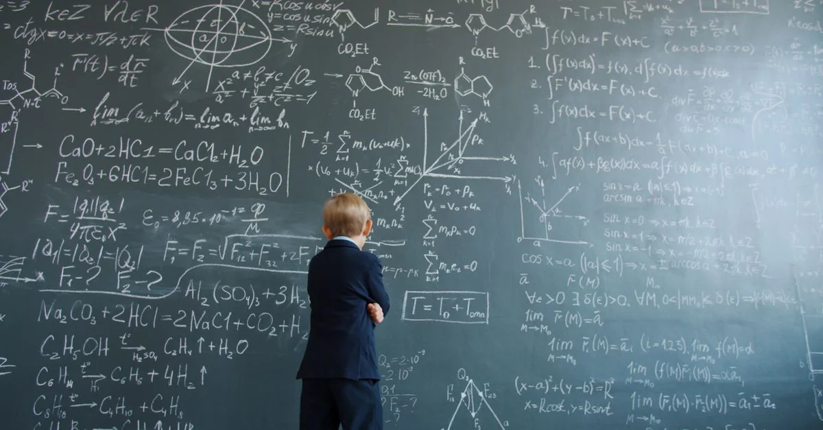 Un enfant en costume étudie des équations mathématiques complexes sur un tableau noir.