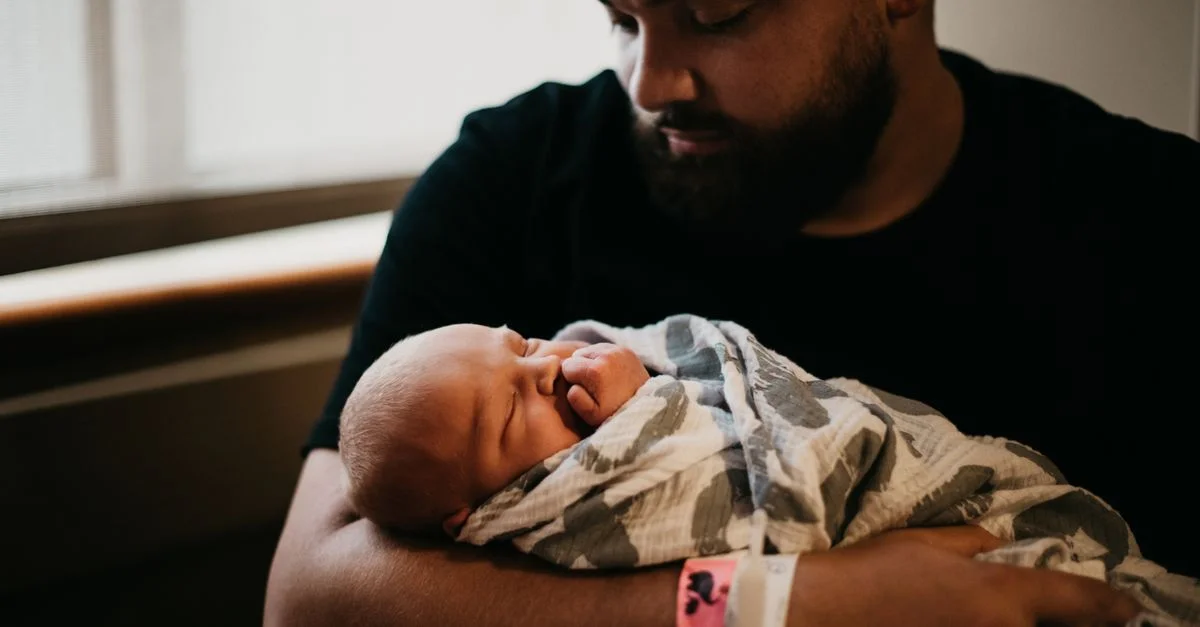 Un momento tierno de un padre sosteniendo a su recién nacido envuelto en una manta en el interior.