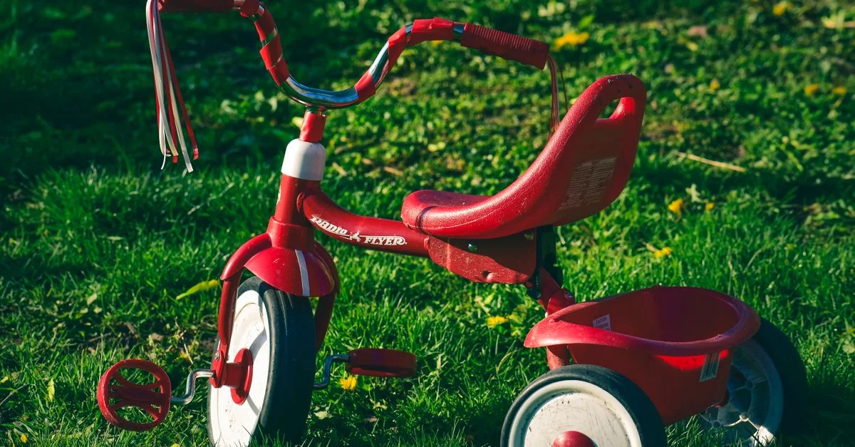 Triciclo rojo vibrante aparcado en un césped soleado, perfecto para recuerdos nostálgicos de la infancia.