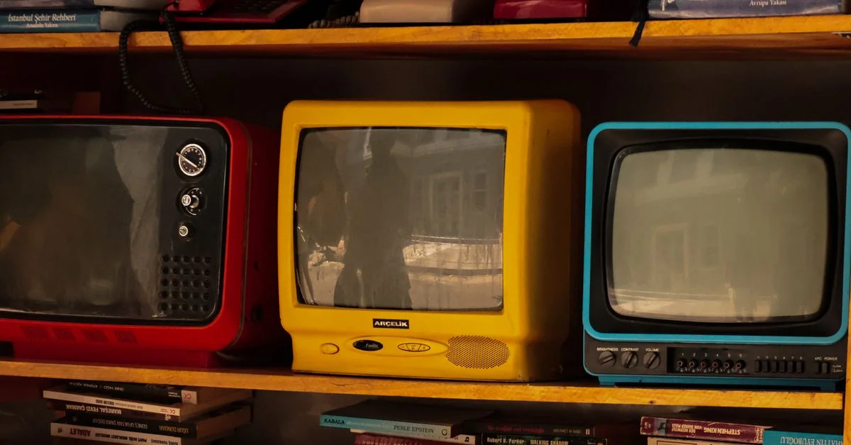 Una colección de televisores retro antiguos y teléfonos viejos sobre un estante de madera, que evocan nostalgia.