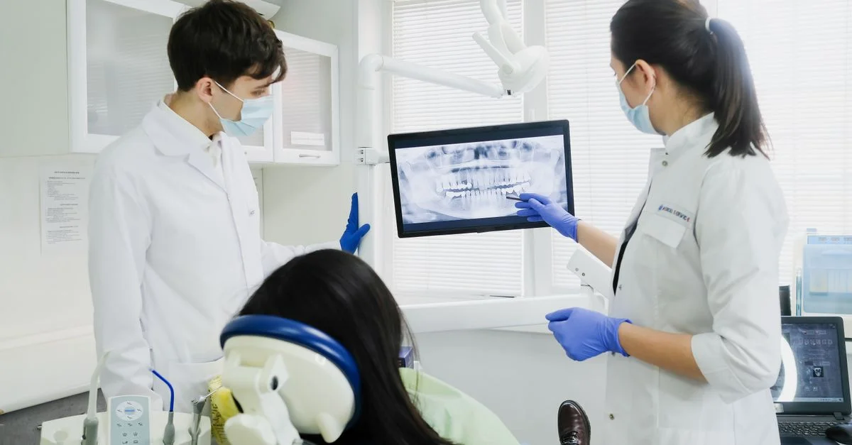 Dos dentistas examinan una radiografía dental con un paciente en un entorno de clínica moderna.