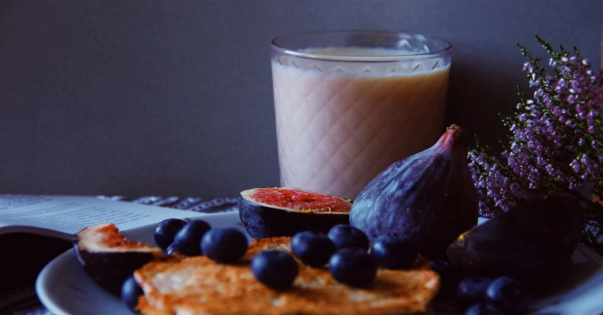 Delicioso plato de desayuno con higos, arándanos y panqueques acompañado de una bebida refrescante.