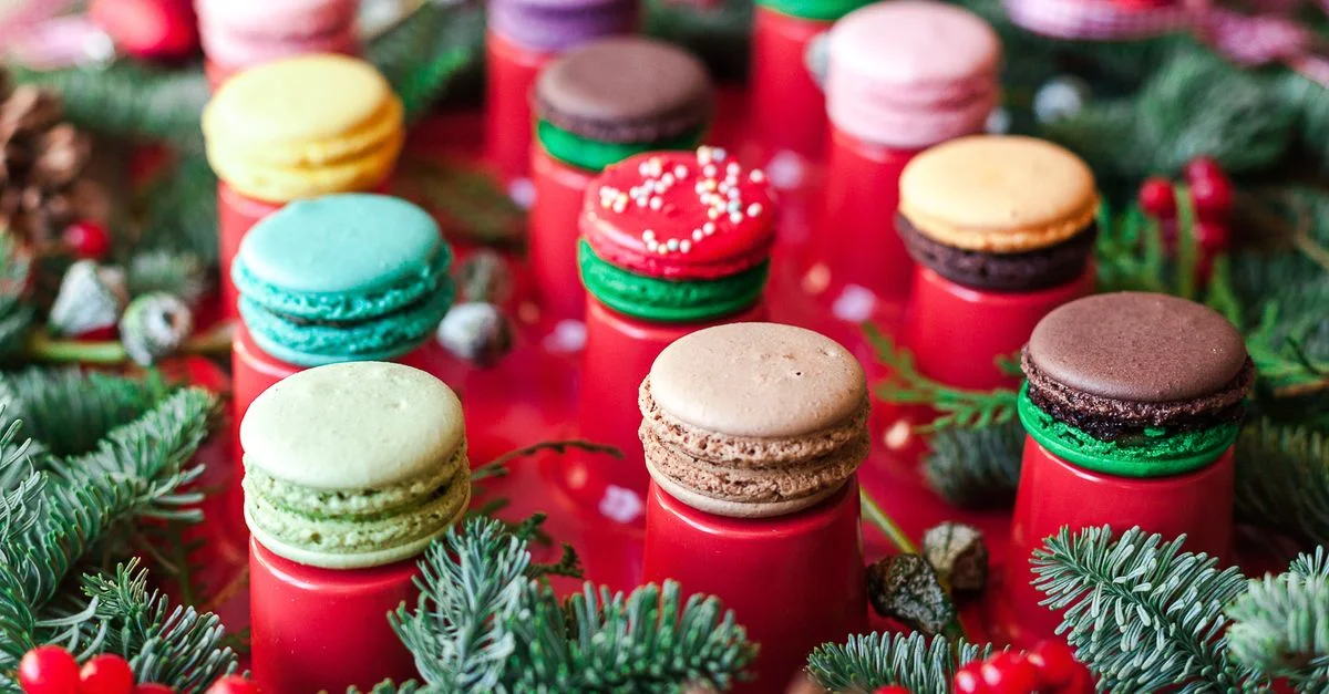 Macarons coloridos rodeados de exuberantes ramas de pino y bayas rojas, perfectos para un dulce festivo.