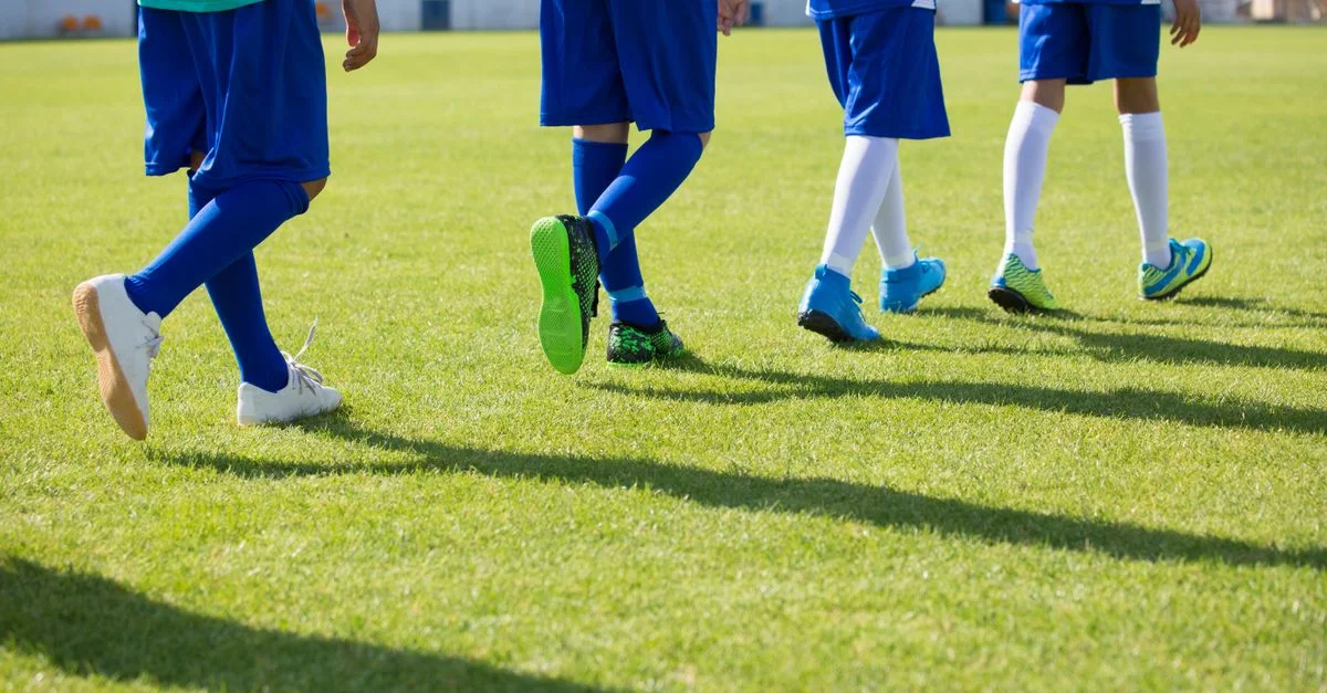 Grupo de niños con uniformes deportivos azules caminando en un campo de fútbol soleado.